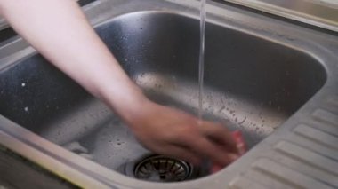 Bir adamın eli, bir mutfak havlusunun yardımıyla çamurdan çiğnenmiş çelikten yapılmış lavaboyu yıkıyor. Mutfak teması. Yakın plan.