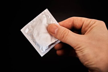 Adamın biri elinde koyu bir arka planda prezervatif tutuyor. Güvenli seks kavramı