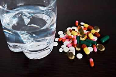 Karanlık bir arka planda bir bardak su ve haplar. Sağlık hizmetleri konusu,