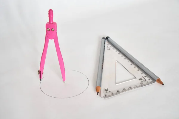 Drawing compass and triangular ruler with two pencils on a white background. View from above.
