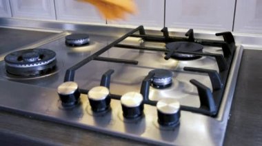 Koruyucu eldiven giyen bir adam paslanmaz çelik bir gaz yüzeyine demir ızgara takar ve onları mutfak süngeriyle pislikten temizler..