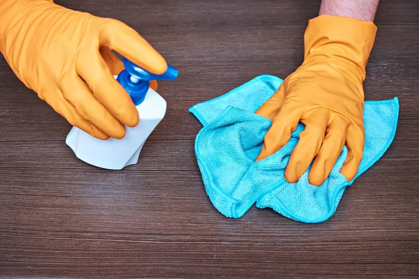 A man in protective gloves wipes the surface of the tabletop with a cleaning agent and microfiber.