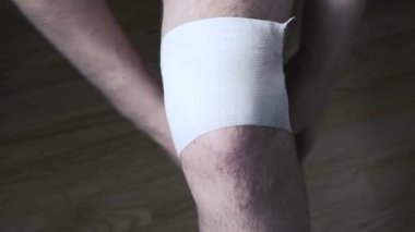 Yaralı bir dizini elastik bandajla saran genç bir adamın yakın çekimi..