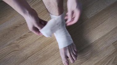 Genç bir adam ayak bileğindeki elastik bandajı çıkarıyor. Tıbbi konular. Yakın plan..