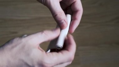 Bir adam elastik bandajı iki eliyle rulo şeklinde çeviriyor. Tıbbi konular. Yakın plan..