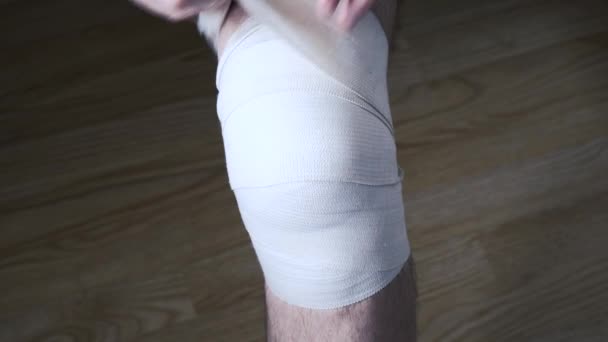 Zbliżenie Młodego Mężczyzny Odkręcającego Elastyczny Bandaż Rannym Kolanie — Wideo stockowe