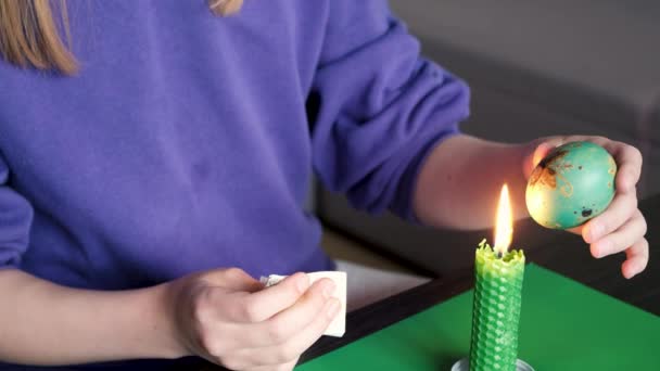 촛불의 도움으로 소녀는 밀랍을 부활절 달걀에서 가져온 냅킨으로 그것을 — 비디오