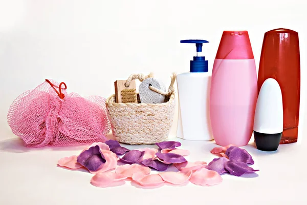 Pembe bez, şampuan, sıvı sabun, aromatik banyo yaprakları, ayak için fırça ve sünger taşı olan bir sepet ve beyaz arka planda diğer tuvalet malzemeleri..