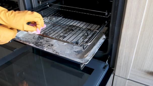 一个戴防护手套的男人用厨房的海绵把烤炉的烤架从烧坏的泥土中清理干净 — 图库视频影像