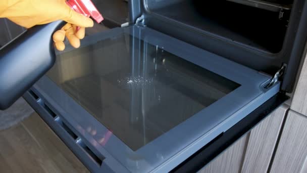 一名戴防护手套的男子在烤箱门上喷洒化学品以清洁玻璃杯 — 图库视频影像
