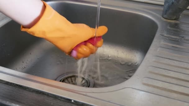 保護手袋を着用する男は それが吸収した汚れから台所のスポンジをきれいにするために水を使用します — ストック動画