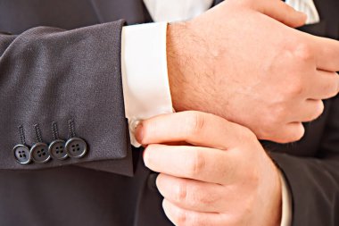 The hand of the groom in a suit adjusts the sleeve of a shirt with a cufflink.