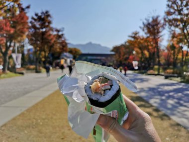 SEOUL, Güney Kore - 24 EKİM 2022: Kore uzun suşisi (Kim-bab) jambonlu, peynirli sebzeli ve içinde sağ elle tutulan şeyler.