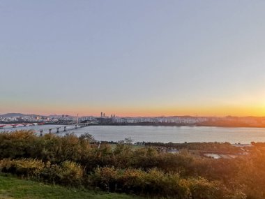 SEOUL, Güney Kore - 24 Ekim 2022: Öğleden sonra köprü, binalar ve Han nehri ve vanilyalı gökyüzü ile sakin bir günbatımı sahnesi.