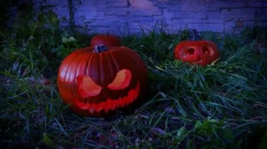 Dark Pumkin Jack O 'Lantern. Bahçesinde ışık var. Arka planda balkabakları var. Sonbahar yaprakları yerde. Çimen, toprak, ateş ve sis. Hayalet dumanı.