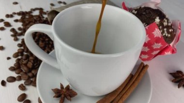 Beyaz bardakta kahve, beyaz ahşap arka planda tarçın, fasulye ve kek.