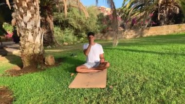 Genç Hintli adam nefes alma teknikleri uyguluyor. Parktaki yoga minderinde seans. Dışarıda daha sağlıklı olmak için rahatla. Yaz mevsiminde Tenerife, Kanarya Adaları 'nda sabah egzersizleri..