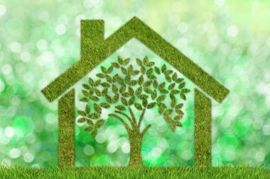 Ekoloji konsepti: ağaç ve sürdürülebilir ev. Bulanık yeşil arka planda çimen desenli bir ev ve ağaç 
