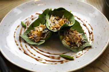 Geleneksel yerel yemek Tayland 'da Bangkok, Tayland' da bir restoranda müşterilere tatlı baharatlı sos sunan kurutulmuş balık ve sebze salatalı Miang Kham veya Savoury Leaf Wraps.