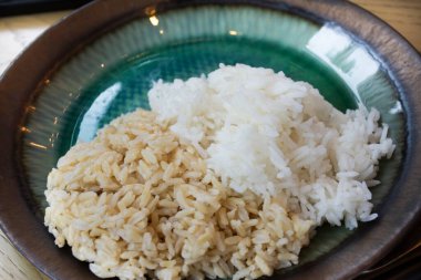 Taylandlı aşçı, sofra üzerinde sofra takımı ya da sofra takımlarıyla lüks seramik tabakta servis edilen esmer pirinç ve beyaz pirinç pişirdi. Müşteriler için yemek masasında sofra takımı var. Bangkok, Tayland 'da bir restoranda içki yiyorlar.