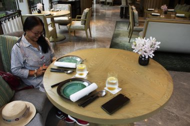 Taylandlı yaşlı kadınlar, Bangkok, Tayland 'da lüks bir lokantadaki modern yemek odasının ana yemek odası arasında oturup limonlu soda içerler.