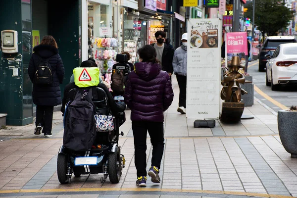障害のある韓国人旅行者は2023年2月18日に韓国の釜山で南浦洞ショッピングセンターまたは南浦洞の光福洞を訪問するための歩道上の自動車車椅子に座っています — ストック写真