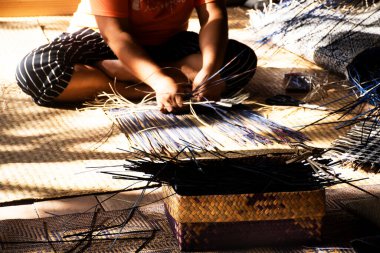 Tayland 'da Phatthalung, Tayland' da Thale Noi 'deki el sanatları atölyesinde özel el yapımı krachut ya da sedge ürünleri satmak için hasır örgü ören profesyonel bir zanaatkar teknisyen.