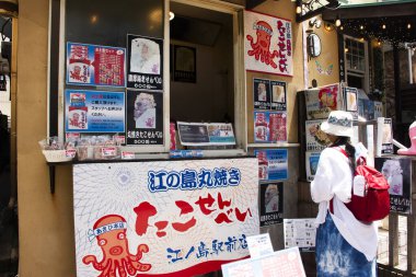 Traveler thai women travel visit and select buy snack cuisine rice cracker with octopus or Senbei traditional japanese food in local Subana street food shop at Kanagawa on July 7, 2024 in Kanto, Japan clipart