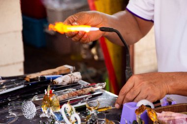 Thai craftsmanship glassmith and artist working making blown glass and blowing glass forming technique inflating molten glass in handmade handicraft market bazzar at Sam Khok in Pathum Thani, Thailand clipart