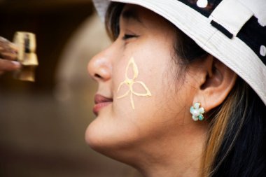 Tayland 'ın yerli çocukları, seyahat eden kadınların yanaklarına pudra tozu sürerek tahta pul yapıştırıyor. Gezginler, her yıl Ratchaburi Tayland' daki Wat Makham Tapınağı 'nda düzenlenen geleneksel kutlamalara katılıyor.