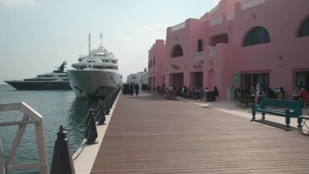 カタールのドーハの旧ドーハ港 ミーナ地区 地元の人々や観光客と一緒にカフェ レストラン クルーズ船を示す午後のショット歩く — ストック動画