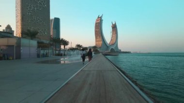 Lusail Corniche, Lusail City 'deki marinada, Katar' da gün batımı çekimleri fıskiyeyi gösteriyor, insanlar arka planda ufuk çizgisiyle geziniyor.