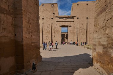 The Temple of Edfu  in Edfu, Egypt external daylight view showing main entrance with visitors and clouds in the sky in background