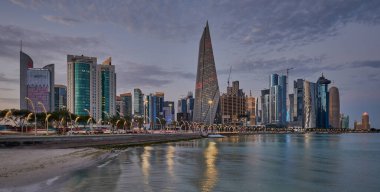 Doha Katar alacakaranlıkta Corniche gezinti güvertesinden gökdelenlerin Arap körfezine yansıyan ışıklarını gösteriyor.