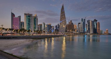 Gün batımında Corniche gezinti alanından Doha Katar gökdelenlerinin Arap körfezine yansıdığını gösteren gökdelenler.