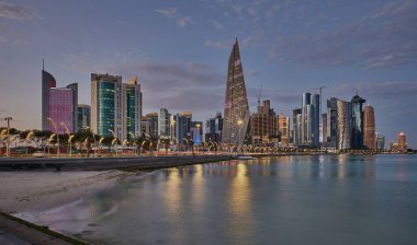 Gün batımında Corniche gezinti alanından Doha Katar gökdelenlerinin Arap körfezine yansıdığını gösteren gökdelenler.