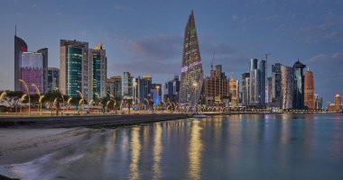 Gün batımında Corniche gezinti alanından Doha Katar gökdelenlerinin Arap körfezine yansıdığını gösteren gökdelenler.