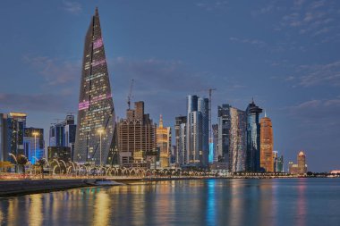 Doha Katar alacakaranlıkta Corniche gezinti güvertesinden gökdelenlerin Arap körfezine yansıyan ışıklarını gösteriyor.