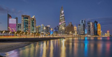 Doha Katar alacakaranlıkta Corniche gezinti güvertesinden gökdelenlerin Arap körfezine yansıyan ışıklarını gösteriyor.