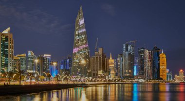 Gece Corniche gezinti alanından Katar silueti Batı Körfezi gökdelenlerinin Arap körfezine yansıyan ışıklarını gösteriyor