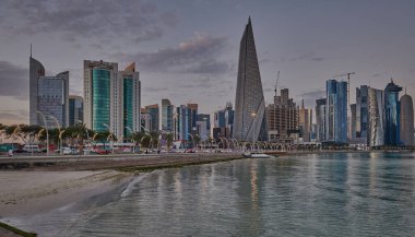 Gün batımında Corniche gezinti alanından Doha Katar gökdelenlerinin Arap körfezine yansıdığını gösteren gökdelenler.