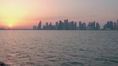 Doha 'daki Mina ilçesinden Doha silueti (Eski Doha limanı), Katar günbatımı Batı Körfezi gökdelenlerini ve arka planda bulutlarla güneşi gösteriyor