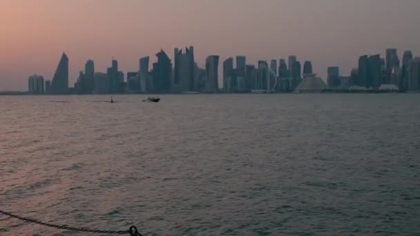 バックグランドの西湾の高層ビルの前にアラビア湾のドウボートを示すショットでズームコーニッチな遊歩道の夕日からドーハのスカイライン — ストック動画