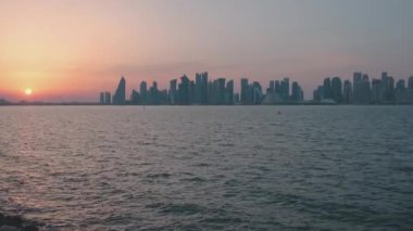 Doha 'daki Mina ilçesinden Doha silueti (Eski Doha limanı), Katar günbatımı Batı Körfezi gökdelenlerini ve arka planda bulutlarla güneşi gösteriyor