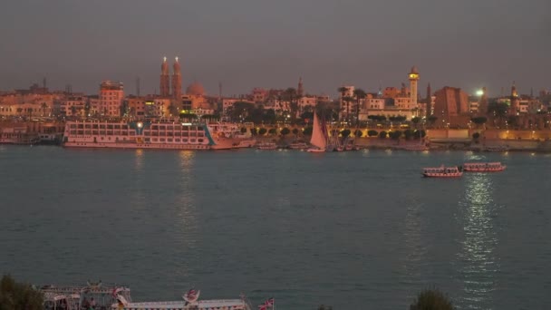エジプトのルクソール西岸からナイトショットフェルーカスとクルーズ船とナイル川を示しています — ストック動画