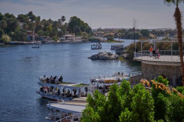 Aswan, Mısır 'daki Nil nehri öğleden sonra çekimleri Aswan Botanik Bahçesi' nden arkadaşlarla ve nehirde teknelerle manzarayı gösteriyor.