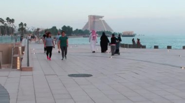 Doha corniche gün batımında yakınlaşıyor. Batı körfezindeki gezinti alanını yerel halk ve ziyaretçilerle gösteriyor.