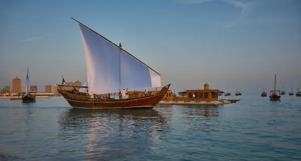卡塔尔多哈的卡塔拉第13届传统独桅帆船节 夕阳西下 展示了在阿拉伯湾悬挂参加国国旗的传统独桅帆船 图库照片