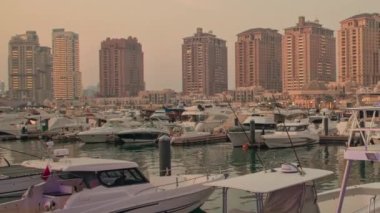 İnci, Doha, Katar 'da Porto Arabistan Limanı' nda çekilen günbatımında marinaya yanaşmış lüks yat ve tekneler, arka planda insanlar ve konut binaları görülüyor.. 