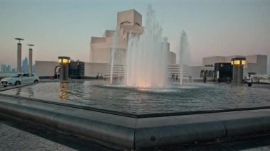 İslam Sanatları Müzesi, Katar dış çekimleri günbatımında ön planda fıskiyeyi ve arka planda müzenin ana girişini arabalarla ve yürüyen insanlarla gösteriyor.